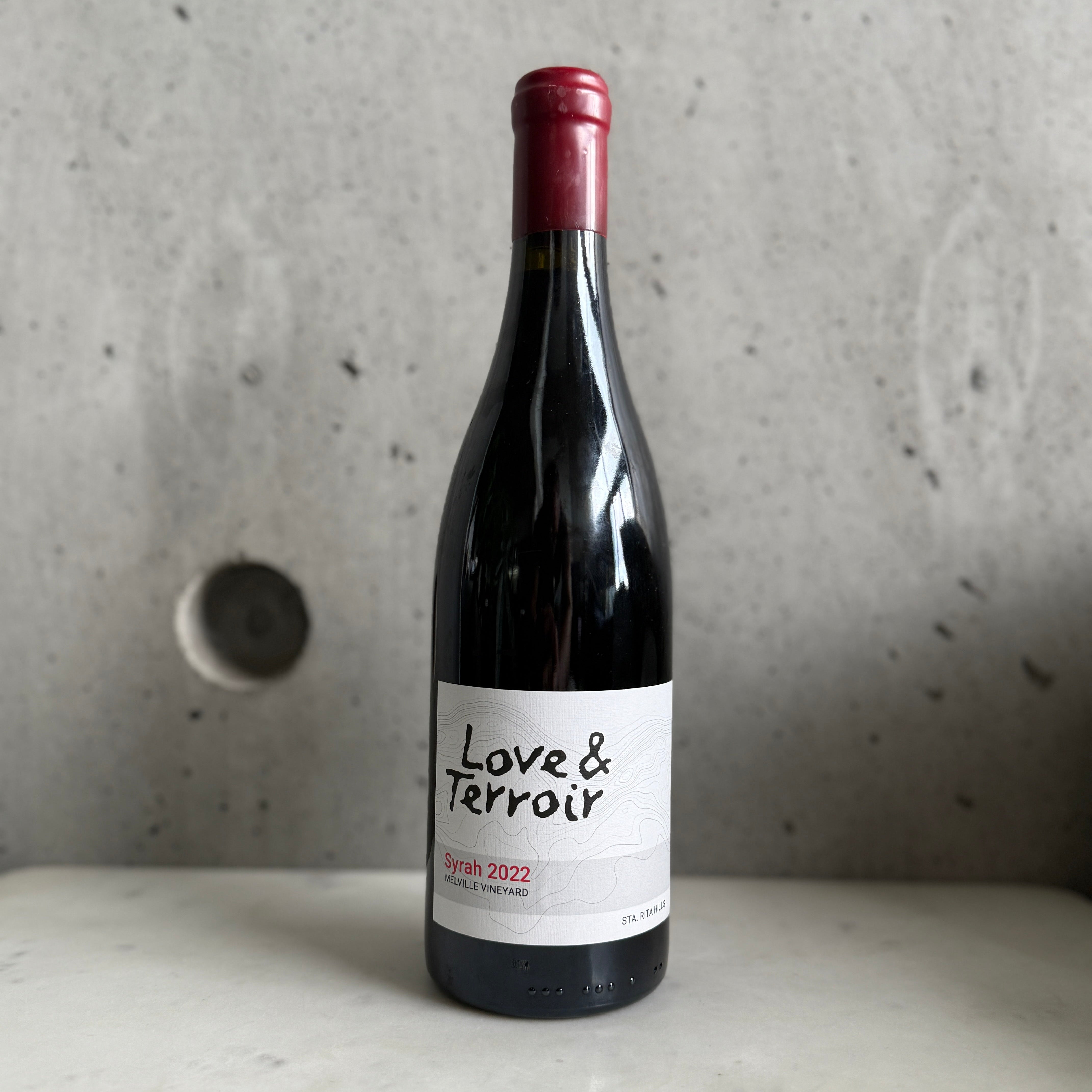2022 Love & Terroir Syrah on a concrete surface with a gray background